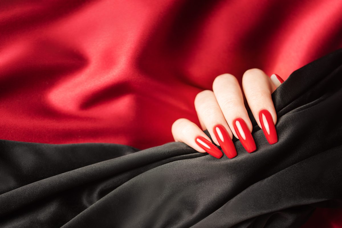 Hands of young girl with red manicure on nails holding black satin cloth on black background