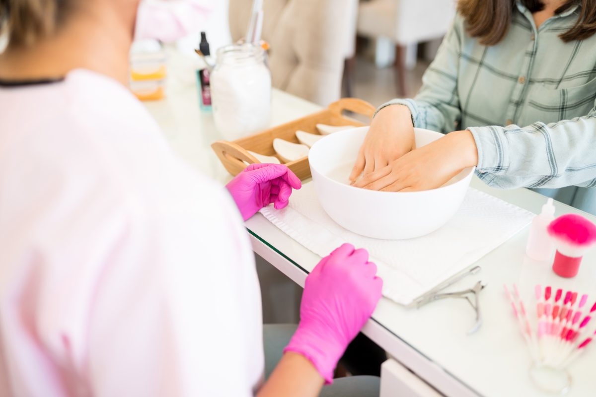 Employee servicing female client with hands in bowl at nail salon. DIY Nail Care/