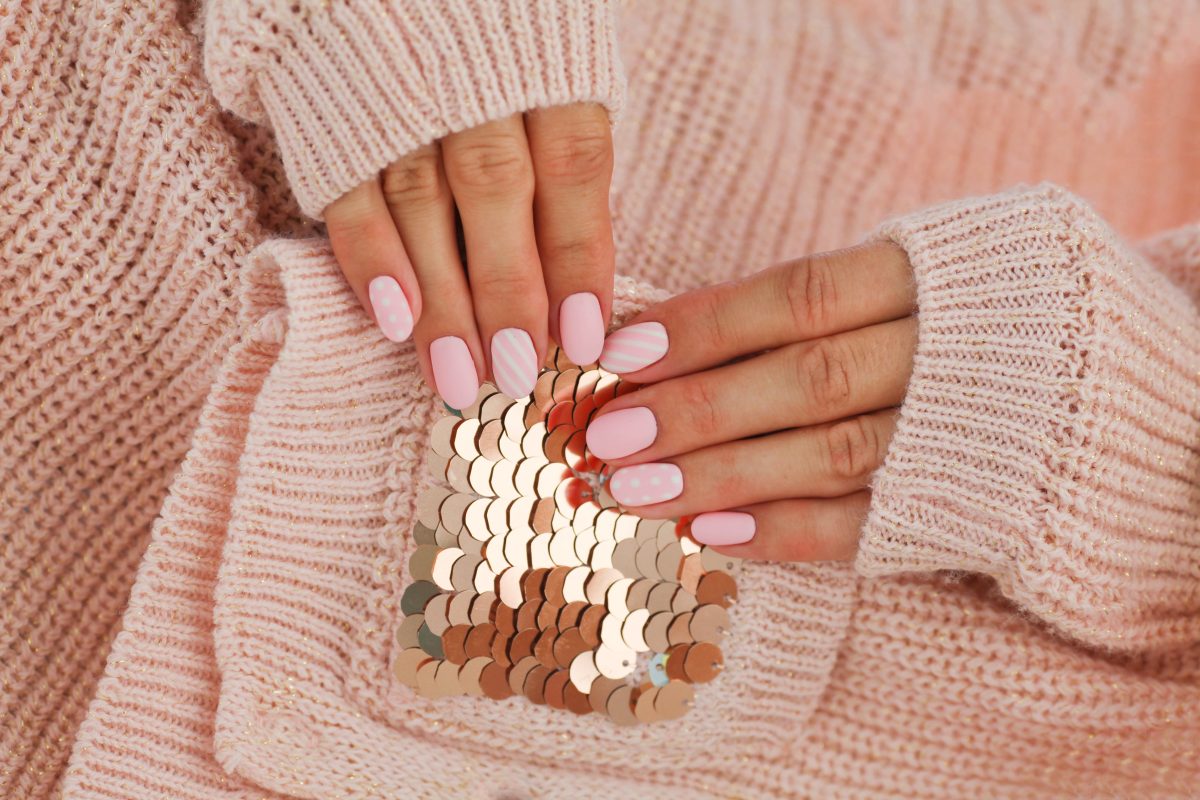 Female hands with beautiful oval-shaped nails, matte pink manicure close-up on a pink knitted sweater background. Shellac. Copy space