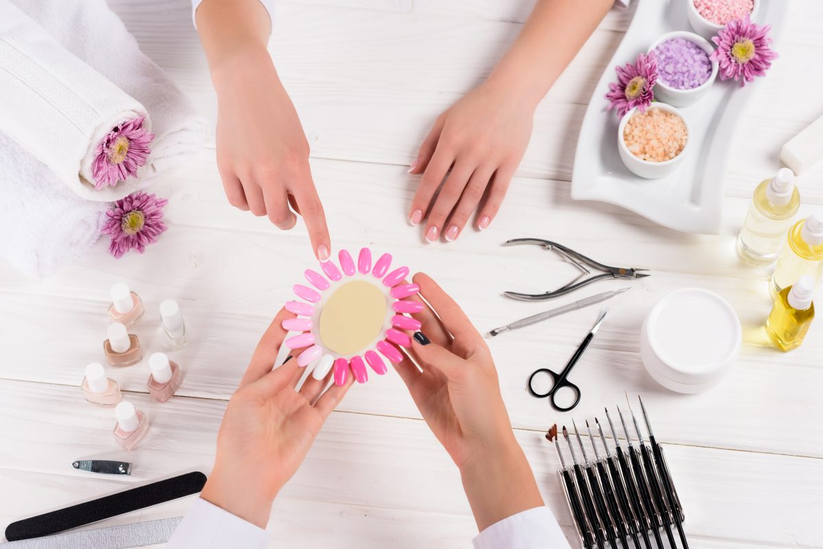 DIY Nail Care. top view of woman pointing on samples of nail varnishes in hands of manicurist at table with nail