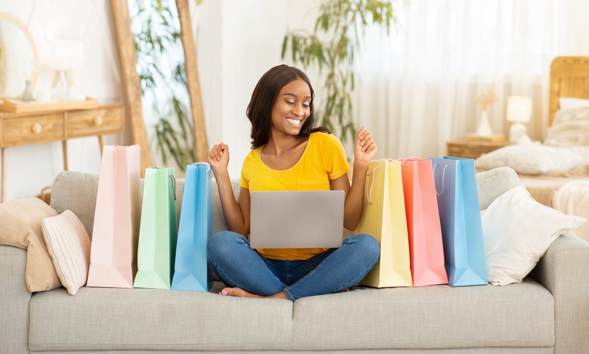 Top 3 Online Nail Supply Stores Canadians Trust in 2025. Cheerful African American lady with laptop computer and shopping bags purchasing via internet at home. Smiling black woman buying goods online while sitting on sofa indoors. Panorama