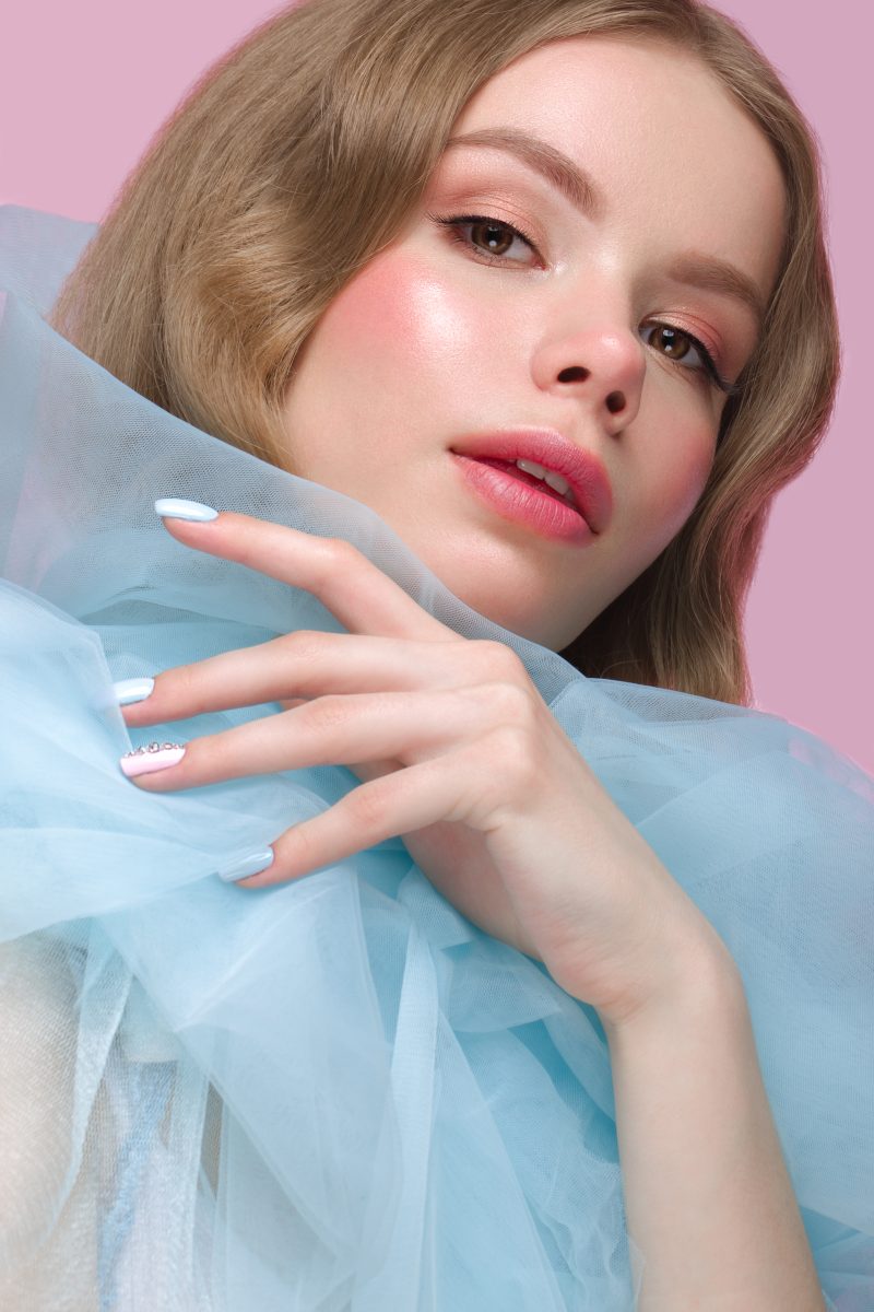 Beautiful girl with light make-up and gentle manicure in blue clothes. Beauty face. Design nails. Photo taken in studio on pink background. 2025 nail color trends. 2025 nail shades. 2025 nail polish trends.