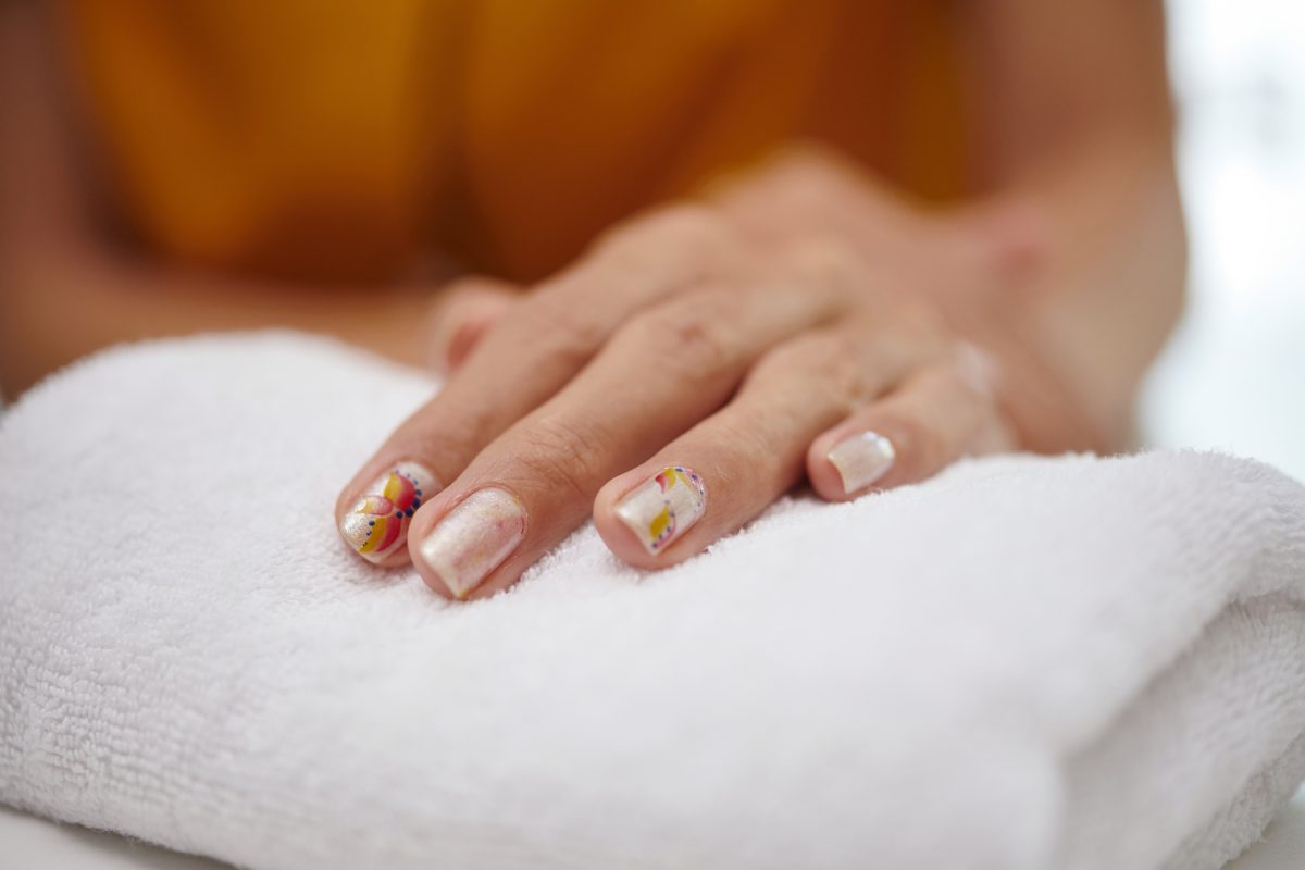Close-up of hands with manicured nails resting on white towel displaying intricate nail art with soft background providing a serene atmosphere
