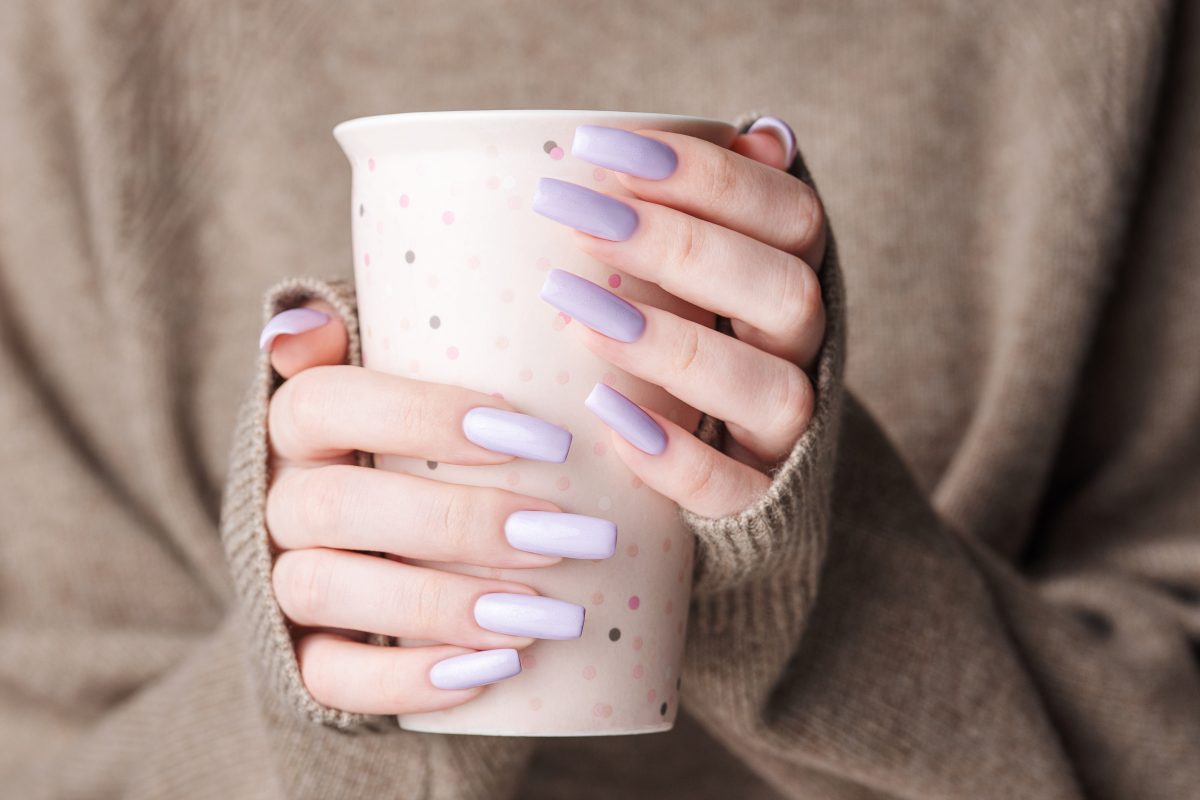 Trendy female manicure. Woman's hands with  violet manicure  holding a cup of tea.  Cozy winter or autumn concept. 2025 Nail Color Trends.