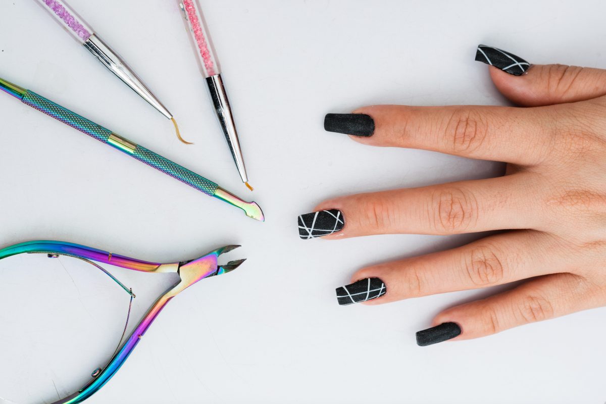 2025 Nail Color Trends. Hand of a girl with her nails made in polygel on a white background and next to her the ideal elements for a basic manicure. cuticle nippers, cuticle pusher and fine painting and design brushes