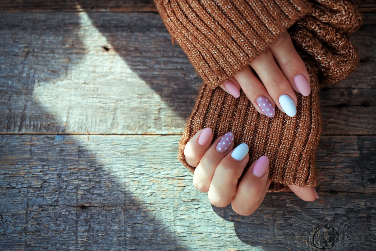 Women is hands with a beautiful manicure, in a knitted sweater on a wooden background in. Autumn trend, polish beige and white polka dots on nails with gel polish, shellac. Copy space.