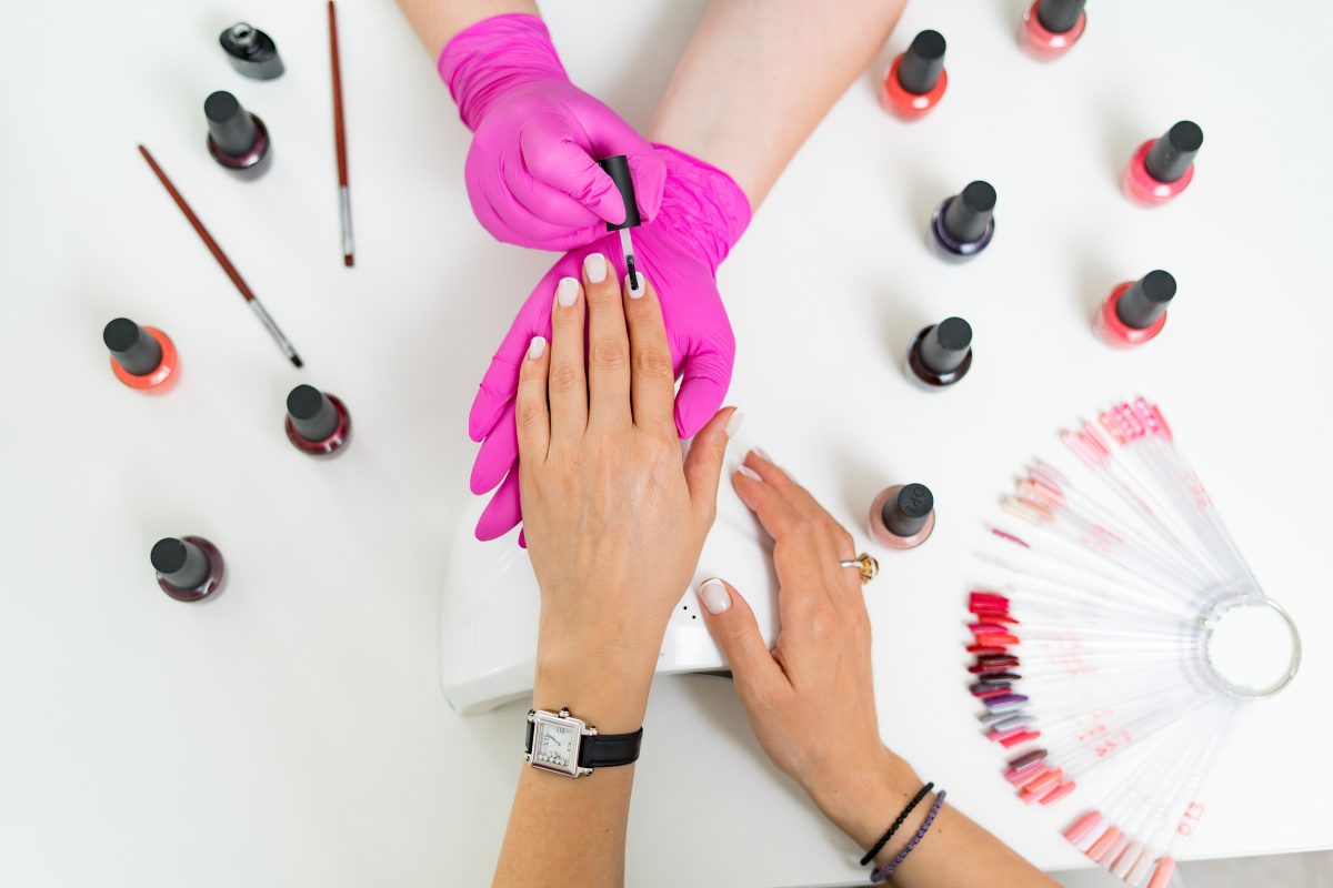 Close up details of woman hands in pink gloves making manicure in luxury beauty salon with modern equipment, soft colors, nail service, perfect client hands.