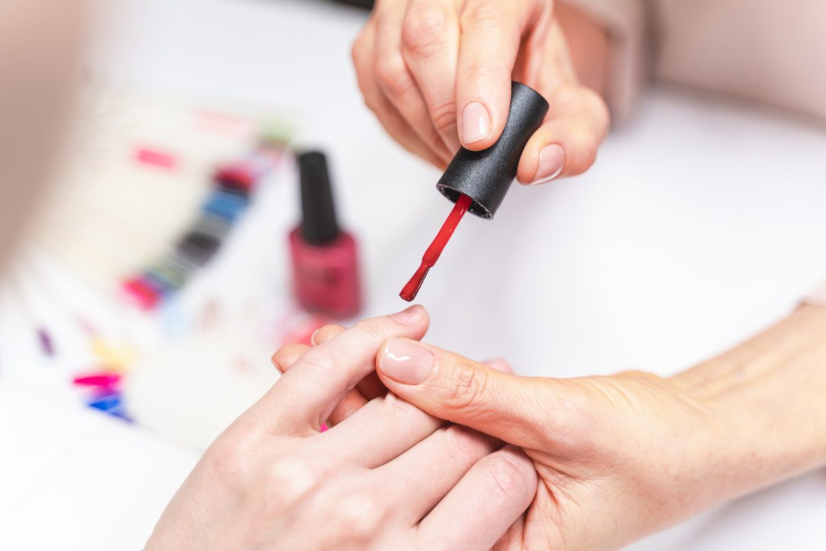 Young client sitting opposite her master while doing manicure in beauty salon, good quality of service