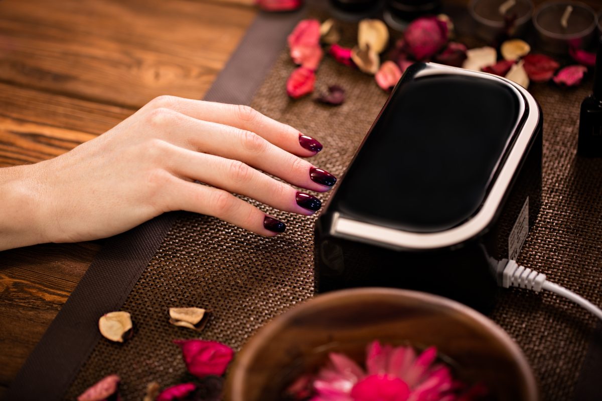 Closeup finger nail care by manicure specialist in beauty salon. Manicurist clear cuticle professional electric Dryer for manicure and pedicure.