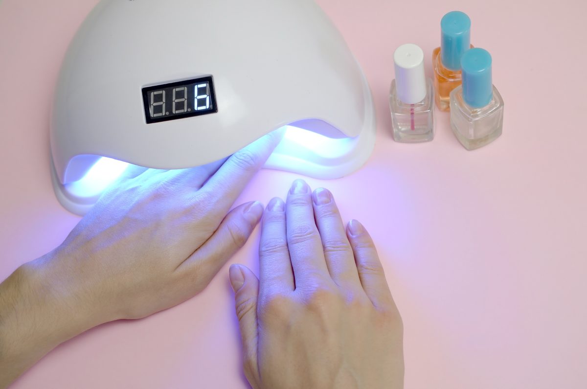 Hands of young woman at manicure procedure close up on pastel pink background. Woman Nail Polish process. Female using shellac uv led lamp for quick drying