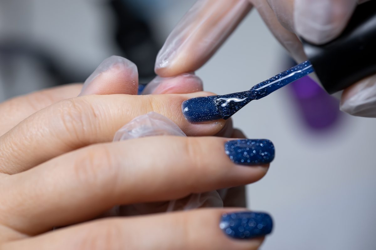The manicure master performs the final stage of applying gel polish to the nail surface with a brush