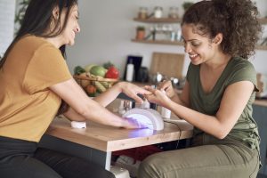 Two women making nail beauty treatments at home. Curing Gel Polish.