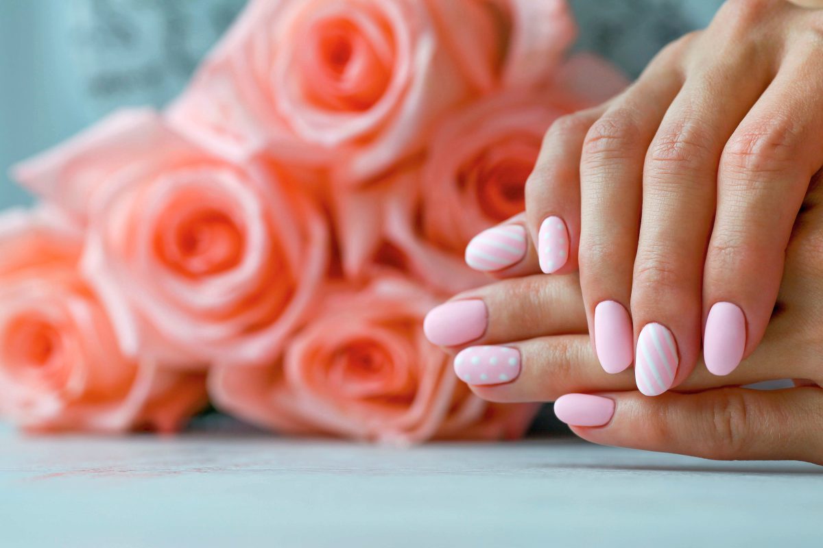 Beautiful pink matte manicure against the background of pink roses. Gel silk, oval-shaped nails.