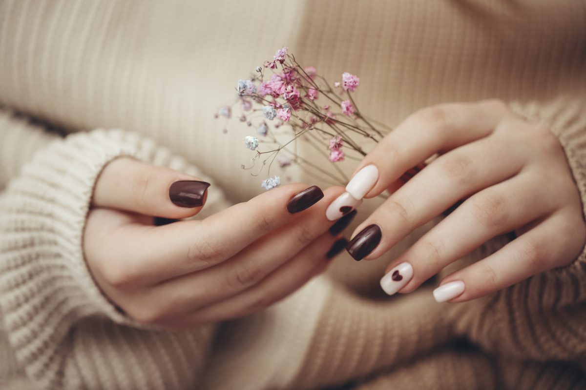 Close up view of beautiful female hand with fashion manicure nails holding hypsophila flowers, white and dark red gel polish, hearts design, on wooven background. Romantic design