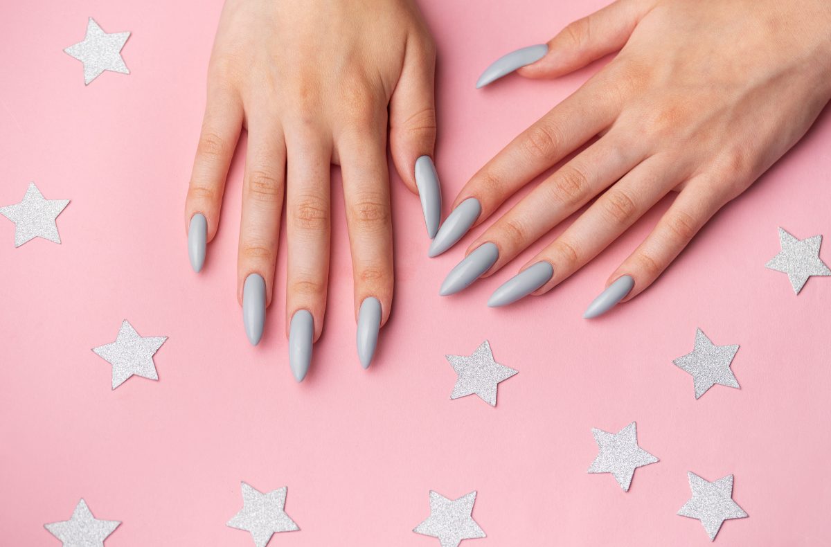 Hands with grey manicure on a pink background with silver stars