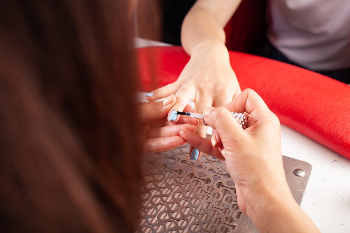 The woman covers the client's nails with a transparent varnish fixer. The process of manicure in a beauty salon. The master of manicure puts in order the nails of the client.