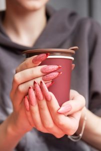 Woman holding an insulated cup, showcasing long nails with red ombre manicure