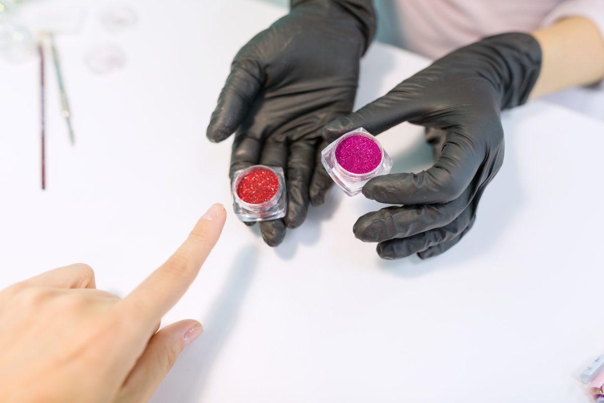 Hands of the manicurist show sparkles, crystals for nails.