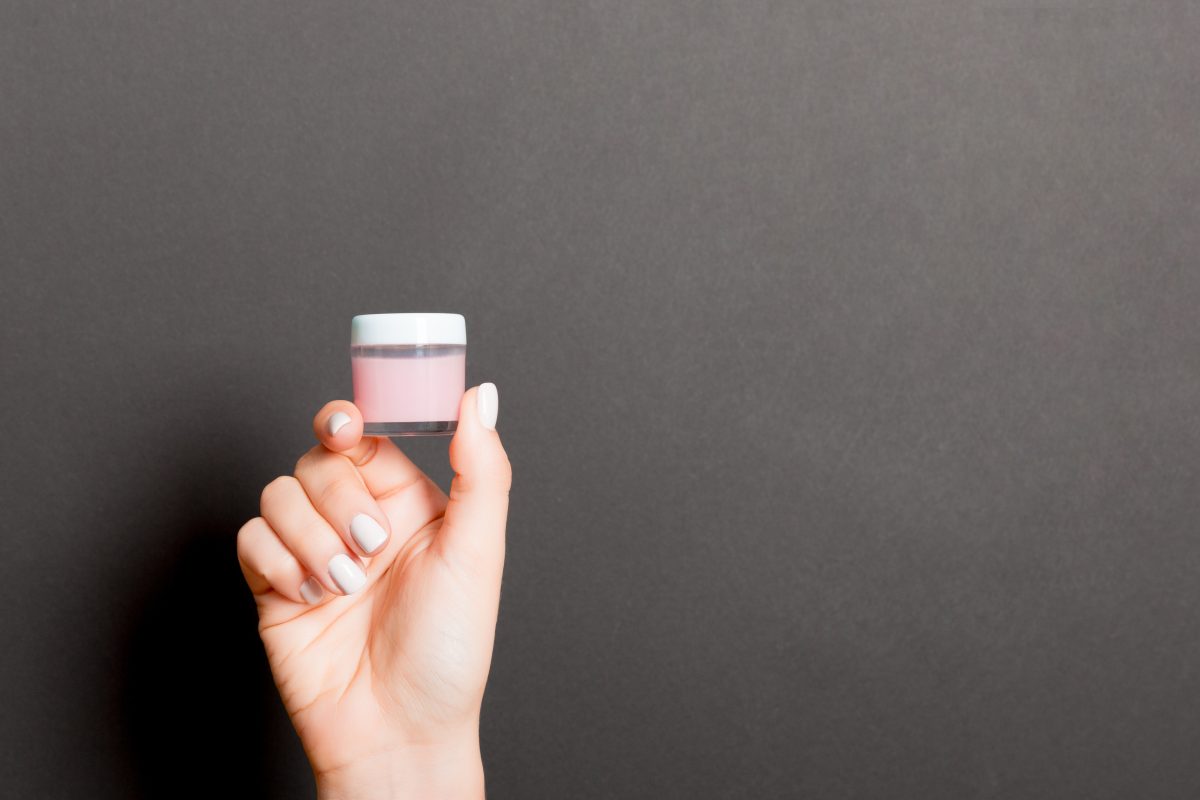 Female hand holding cream bottle of lotion isolated. Girl give jar cosmetic products on black background. Gel vs. Dip Powder