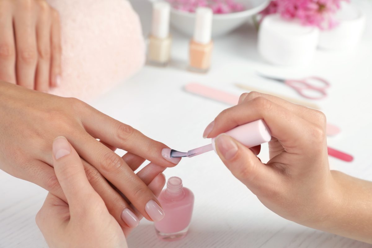 Manicurist applying polish on client's nails at table, closeup. Spa treatment. Gel vs. Dip Powder
