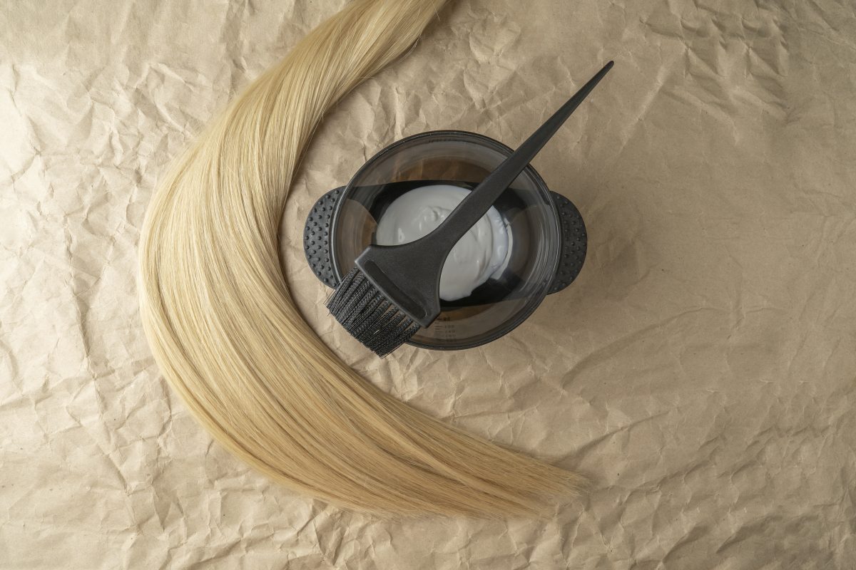 A strand of blonde hair lying next to the brush for coloring and hair dye. Professional Hair Color.