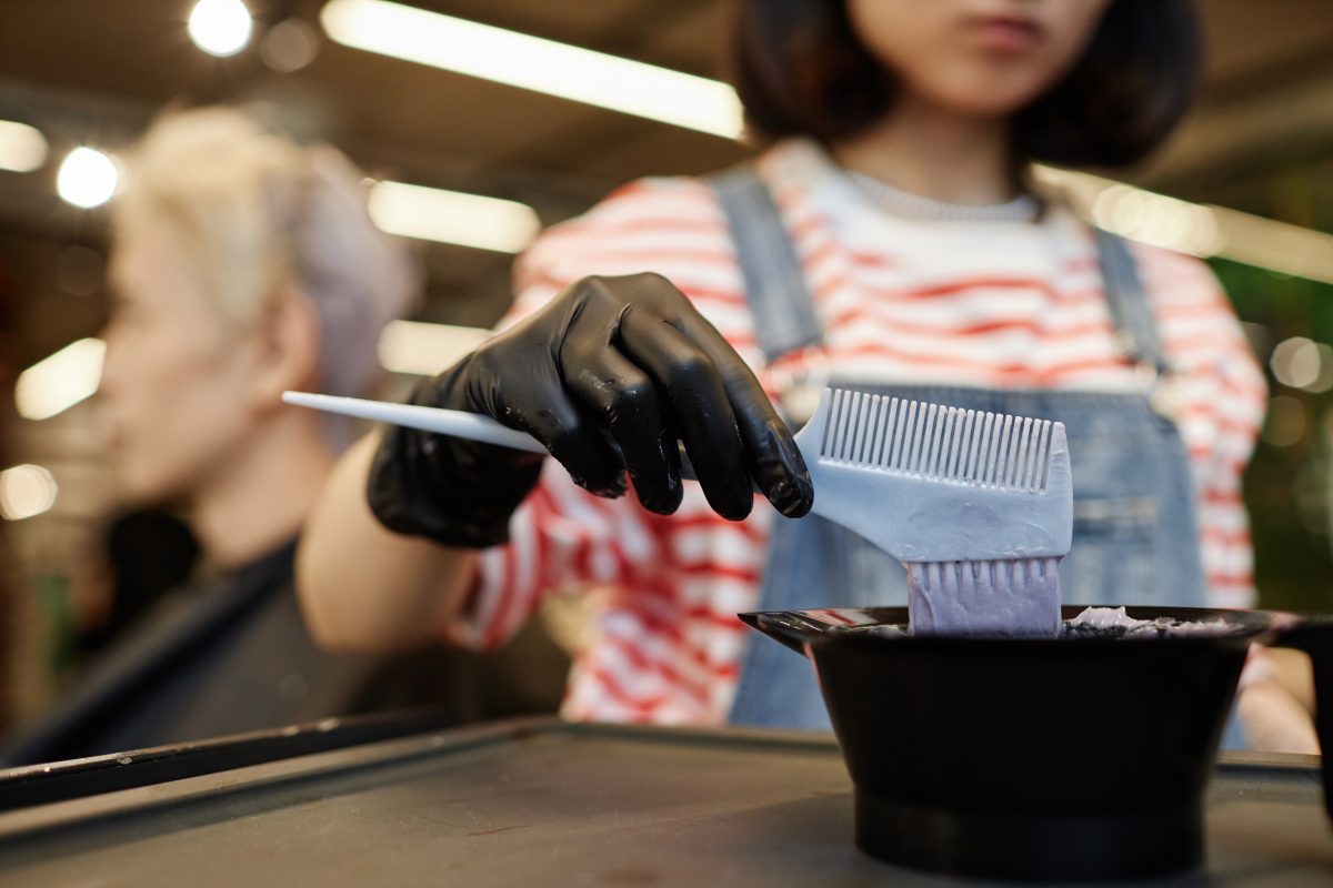 Closeup of a hairstylist mixing lightening solution in plastic bowl at beauty salon, copy space