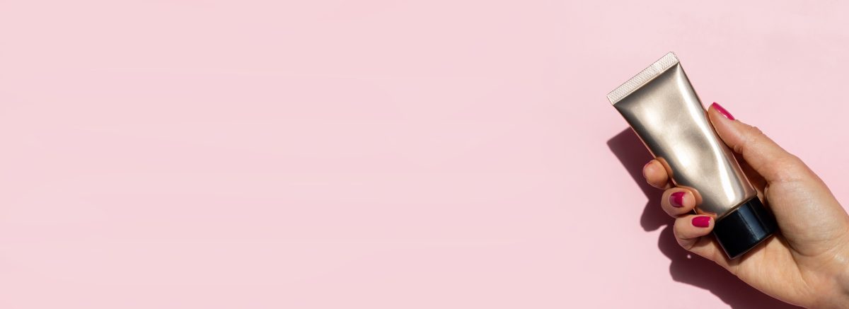 Close-up beautiful female hand with red nails holding cream tube on pink background with copy space. Manicure in trendy of 2023 year color viva magenta. Concept hand care, anti-wrinkles, anti-aging cream and spa salon. Soft skin, skincare concept.