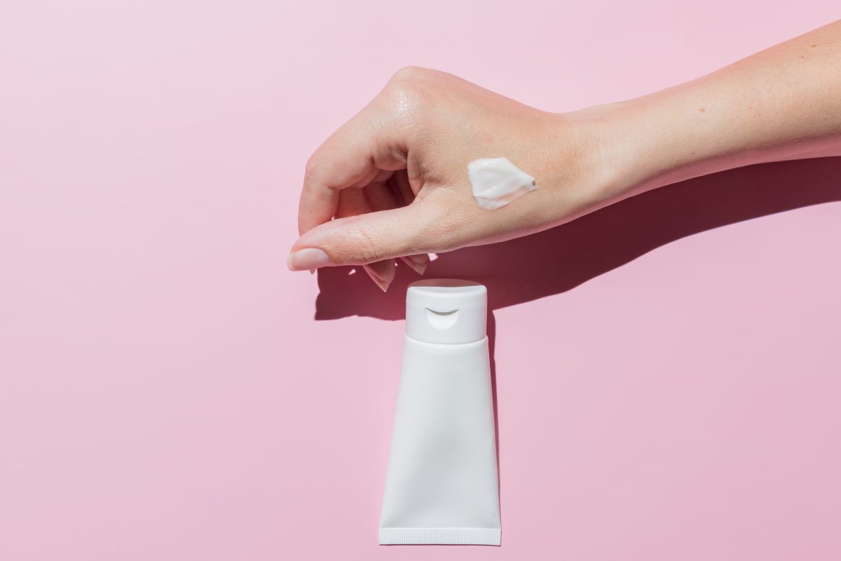 Female hand applies cosmetic skin care moisturizer cream on a skin on pink background. Cosmetic mockup for designers.