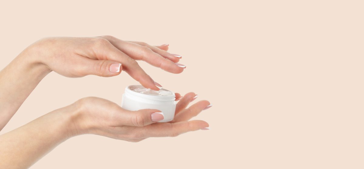 Female hand holding cosmetic cream jar on beige background. Copy space, close up