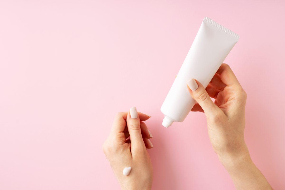 Womans hands with cream on pink background, beauty cosmetology and care concept top view