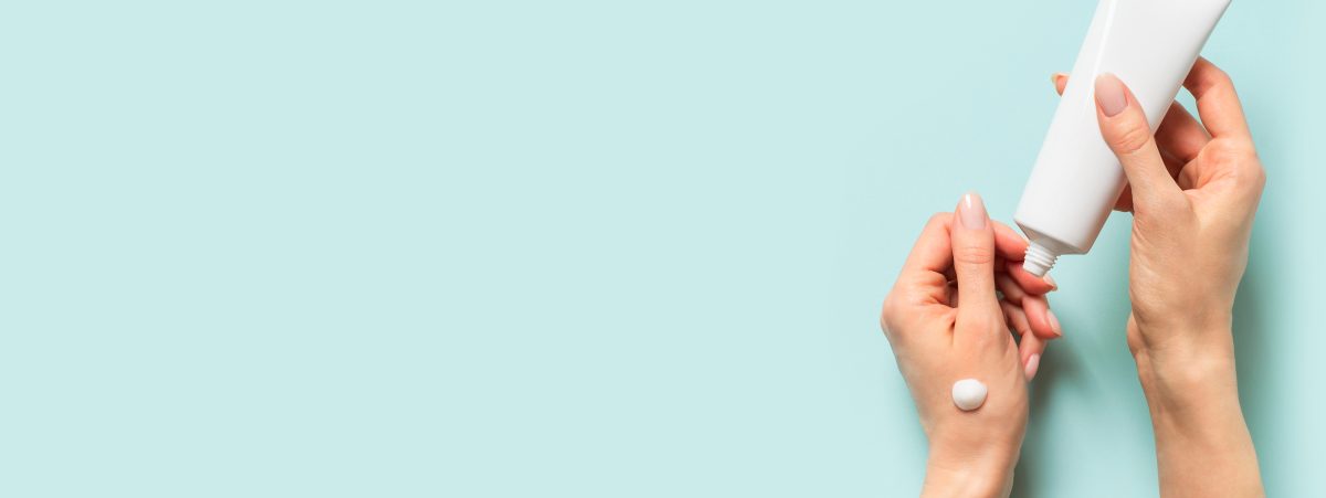 Beauty concept with woman hand and cream tube on blue background, flat lay, copy space, top view