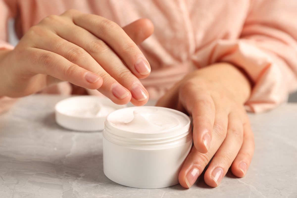 Woman applying hand cream at grey table, closeup