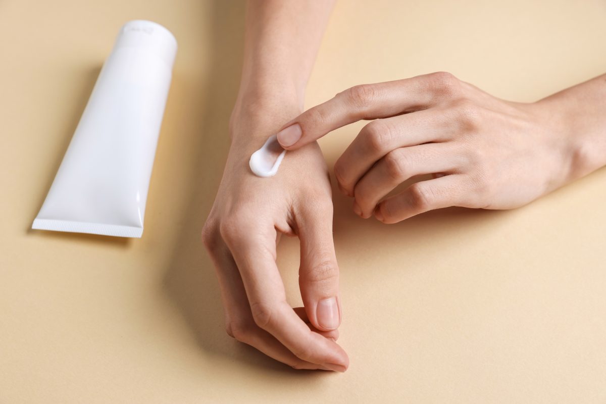 Woman applying hand cream on beige background, closeup