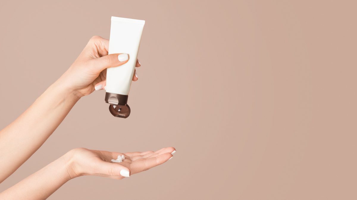 Closeup view of young female applying hand cream on pink background, copy space. Panorama