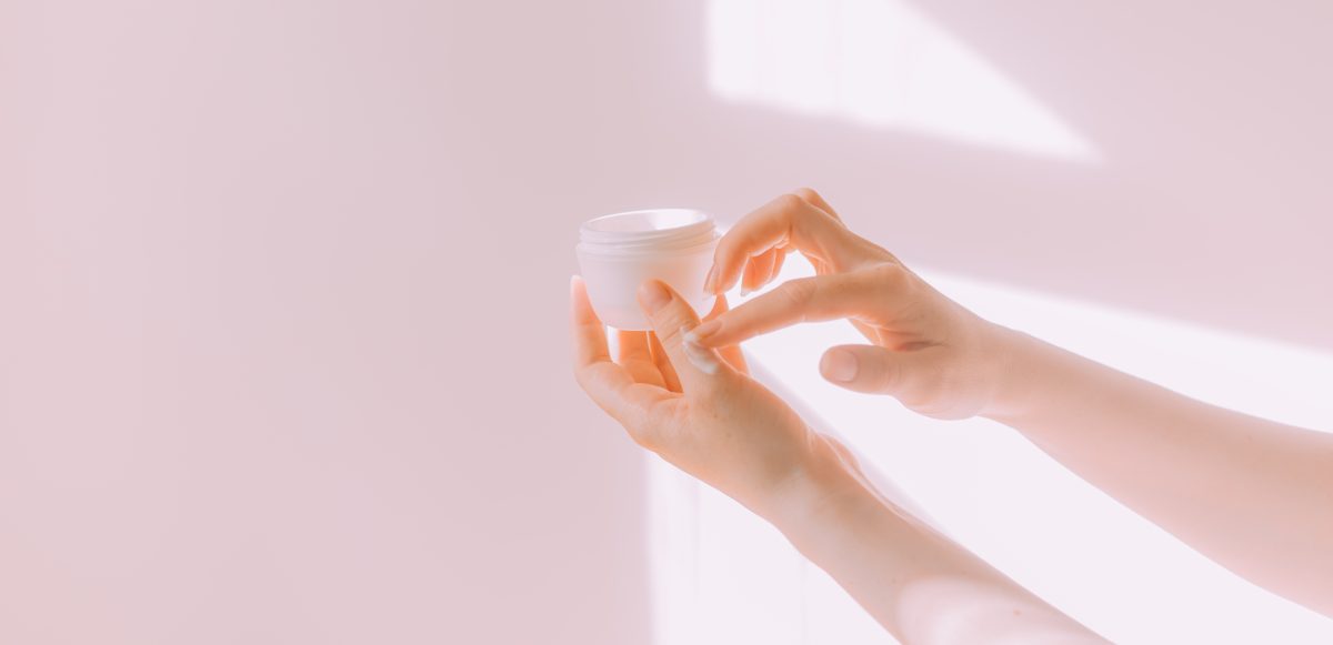 Woman using hand cream from jar on her hands.