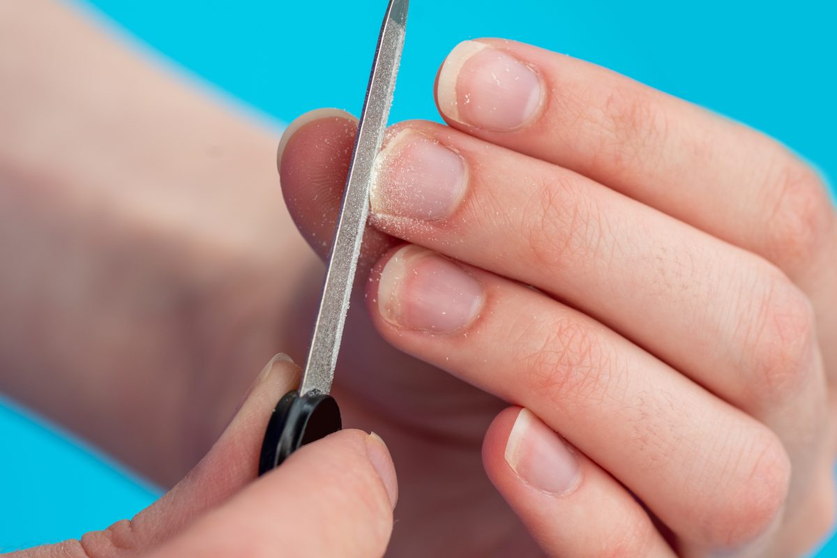 Hands of a caucasian woman polishing her nails with a nail file on a blue background, close-up, copy space. The idea of self-care of nails, hands.