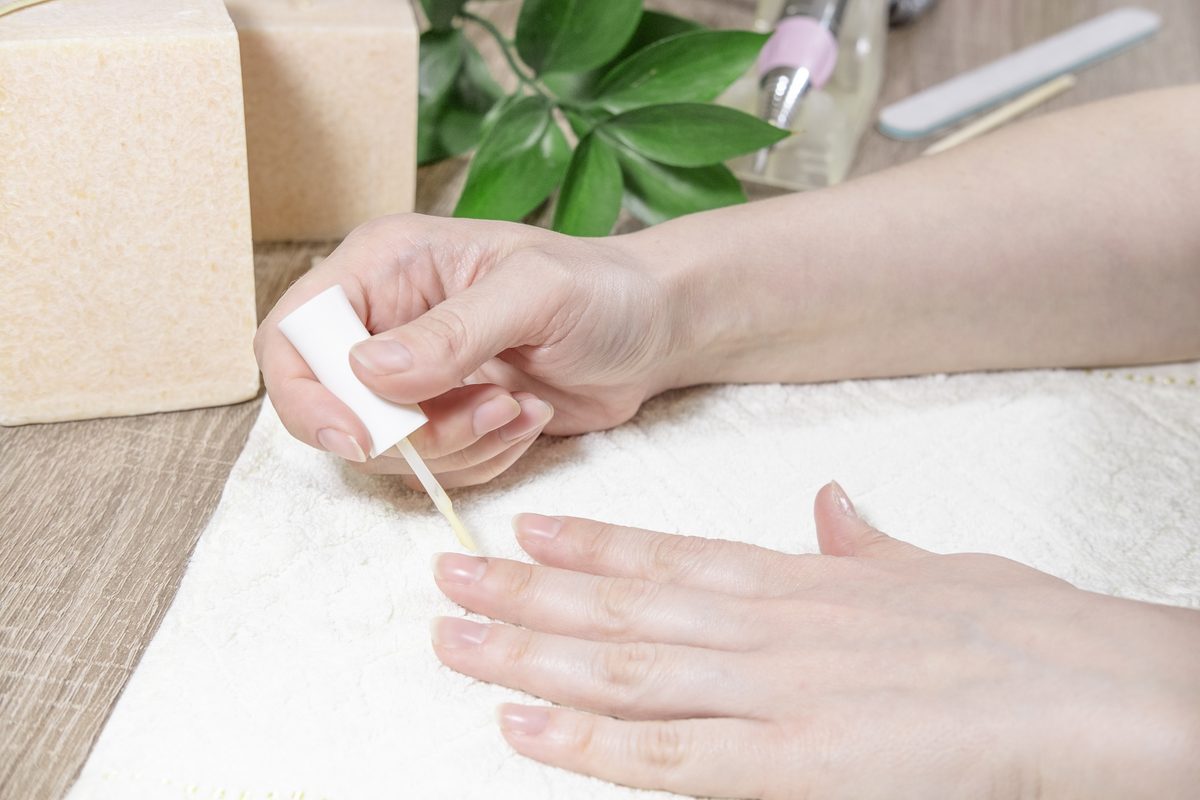 A woman manicurist treats her nails with a protective coating, nail polish or gel polish using a beige transparent product in a beauty salon. Manicure process or nail polish operation close-up.