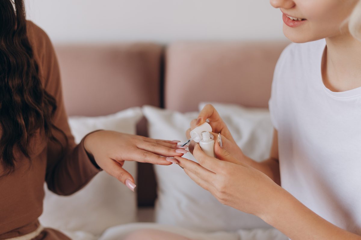 Close up of two pretty girlfriends in pajamas polishing nails, spending time together at home. Lifestyle, beauty, friendship concept